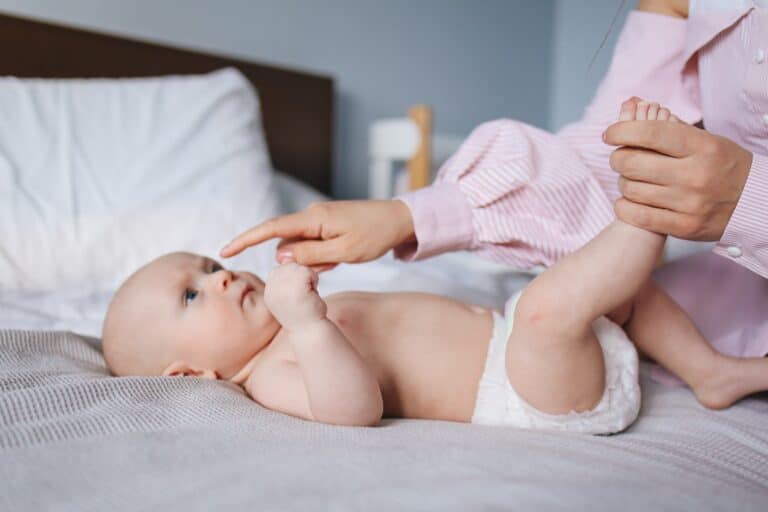 photo of baby on a bed wearing a diaper and an adult arm booping its nose for post about seventh generation diapers reviews